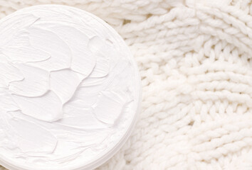 Cream close-up on the texture of a white knitted fabric. Winter cosmetics concept. View from above. Copy space