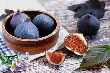 A wooden bowl full of fresh figs on a rustic background