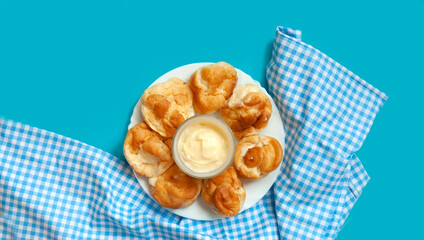 Small round eclairs or profiteroles lie on a blank background. Next to a plate with dessert on the table is a crumb of milk. Copy space