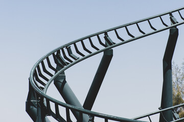 Naklejka premium Curved Rollercoaster at a theme or amusement park empty green metal tracks and on blue sky background.