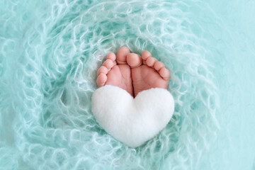 legs newborn baby close up on a blue background with a toy in the form of a heart - obrazy, fototapety, plakaty