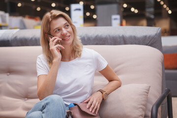 Mature housewife talking on the phone resting on a sofa at furniture store
