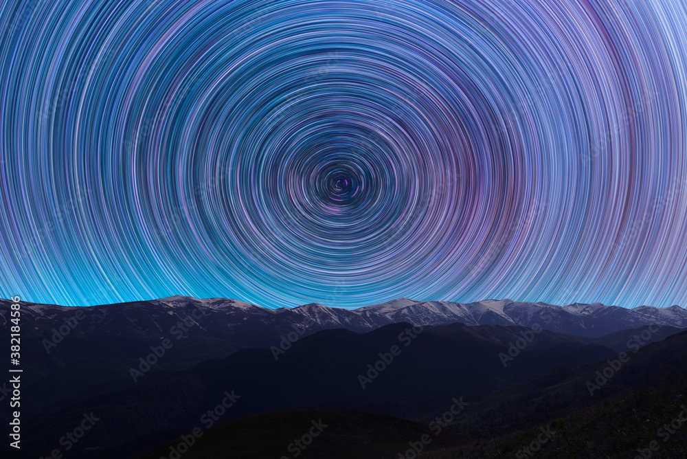 Wall mural Long exposure night landscape. Beautiful mountains and. colorful star trails on the sky. Night time lapse photography.