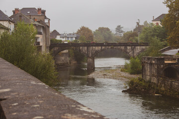 Fototapeta na wymiar Old bridge over the river on rainy day. Cloudy day in medieval village in France. Arched bridge over canal. Autumn landmark. Travel in historical places in France. Countryside with river. 