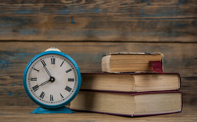 Retro alarm clock and stack of old books over wooden wall background