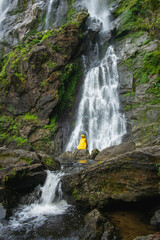 Woman sits on a rock with a beautiful waterfall in front.