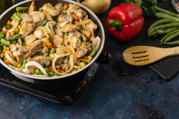 Close-up of pan with frying chicken meat with vegetables for pasta on dark blue background. Background of cooking pasta. Food concept. Restaurant or hotel dish.