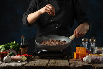 Chef prepares meat in pan wok for cooking traditional mexican tacos. Dark background. Frozen motion. Food concept. Ingredients for dish on the rustic wooden table.