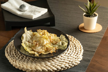 delicious and Juicy, Stir-fried cabbage with fish sauce served in a black dish and decorate the table with and napkin holder and plant.