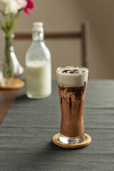 Refreshing summer drinks or beverages, chocolate cocoa latte with chocolate sauce, and cold foam milk on top in a tall glass, on a grey placemat.