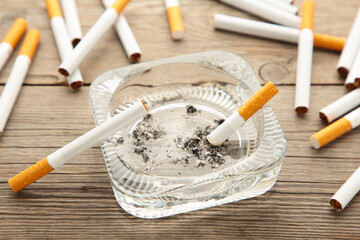 Cigarette butts with ash in ashtray on grey wooden table