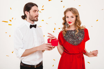 young stylish couple celebrating new year, happy disco party, luxury style, cool outfit, having fun, making presents, holding gift box, surprise, red sexy dress, blond hair, golden confetti in air