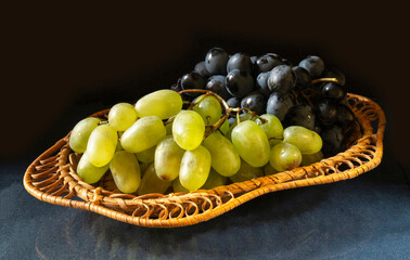 Green and dark grape in plate on table on dark background