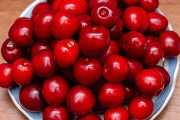 red fresh cherries in a plate on a wooden background