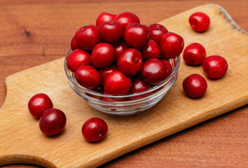 red fresh cherries in glass plate on wooden board on a wooden background