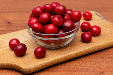 fresh black cherries in glass plate on wooden board on a wooden background