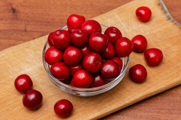 fresh black cherries in glass plate on wooden board on a wooden background