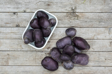 Raw harvested indigo potato tubers on a background of wooden boards.