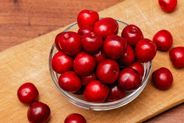 fresh black cherries in glass plate on wooden board on a wooden background