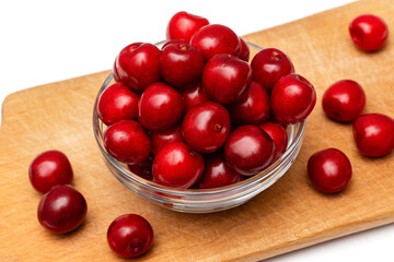 red fresh cherries in glass plate on wooden board on a white background