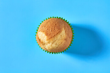 One fluffy muffin in green paper mold on blue background. Top view