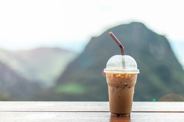 Ice cappuccino coffee on wooden table with blur natural mountain view background.