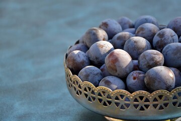 Fresh ripe plums in metal pattern vase on blue background close up