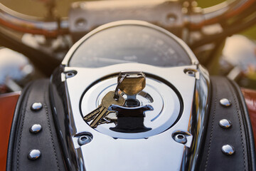 Control panel of classic orange motorcycle with lots of chrome parts and riveted tie, made of genuine brown leather. Keys are in ignition lock Motorcycle is shot at sunset in park