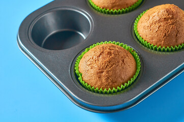Metal mold without one fluffy muffin on blue background