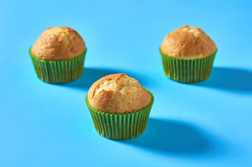 Three fluffy muffins in green paper mold on blue background