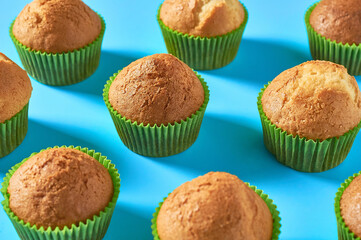 Many fluffy muffins in green paper molds scattered on blue background