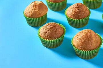Many fluffy muffins in green paper molds scattered on blue background. Space for text