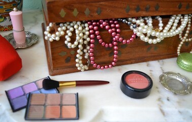 Close-up of a marble feminine dressing table where there is a wooden Indian box with pearl necklaces, eye shadows, makeup, a brush and a lipstick