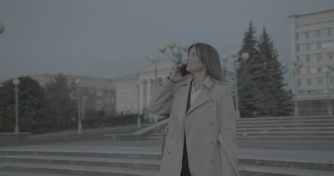 Happy smiling business woman in raincoat and suit walking and talking on phone.