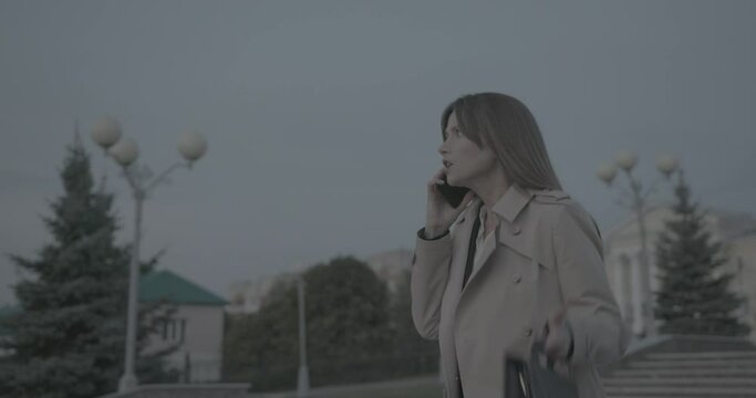 Annoyed nervous business woman in raincoat and suit walking and arguing on phone. Lady feel disgruntled.