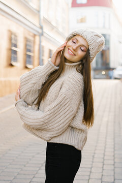 Charming young brown-haired woman on a walk. A beautiful and happy woman in a stylish image in a knitted warm hat. Walking around the city, lifestyle