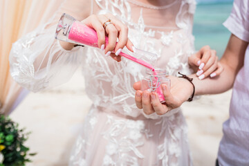 Close up view of bride and groom filling color sand into the jar at the wedding sand ceremony on the paradise beach, Punta Cana, Dominican Republic