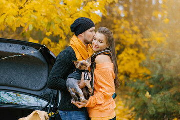 A guy and a girl in love embrace in an autumn Park, a guy holds a cute dog in his arms and kisses his favorite girl