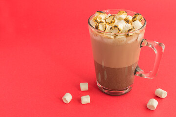 Hot cocoa or chocolate drink with marshmallow in the glass cup on the red background copy space