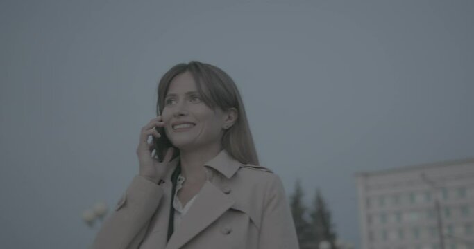 Close up view of happy smiling business woman in a raincoat and suit talking on phone.