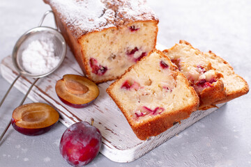 Sponge cake with plums and apples with powdered sugar on a light wooden board on a light background