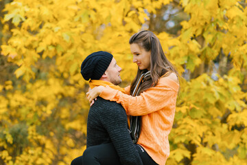 A couple in love embraces each other in the autumn forest. A young man and a girl are walking, a guy is holding a girl in his arms. Travel in the autumn time of the year, at weekends.