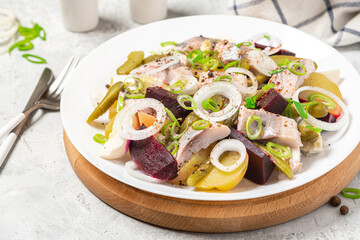 Salad of herring, beets, potatoes, eggs, pickling cucumbers and spices in white plate close up.