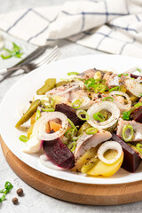 Salad of herring, beets, potatoes, eggs, pickling cucumbers and spices in white plate close up.