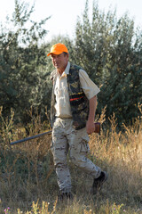 Duck hunter with shotgun walking through a meadow.