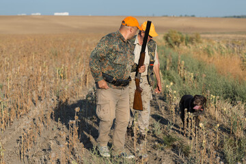 Duck hunters with shotgun walking through a meadow.