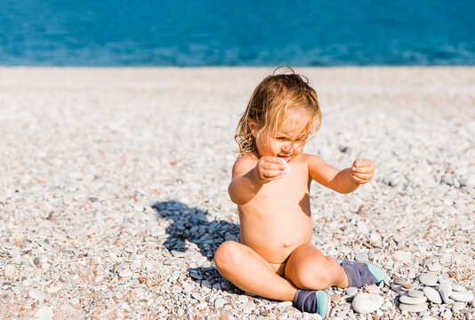 Toddler Girl Playing With Pebbles On Beach