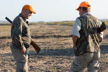 Duck hunters with shotgun walking through a meadow.