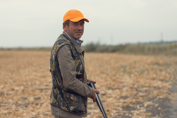 Duck hunter with shotgun walking through a meadow.