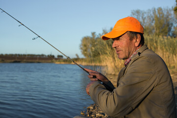 Fishing rod wheel closeup, man fishing with a beautiful sunset.